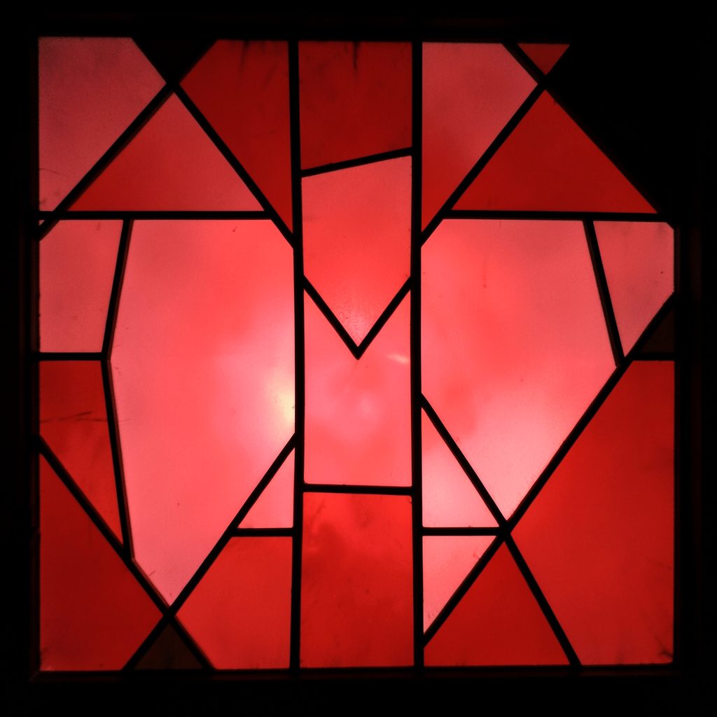 Stained-glass panel with bold black leading, warm amber, dusty rose, and teal segments, atmospheric glow
